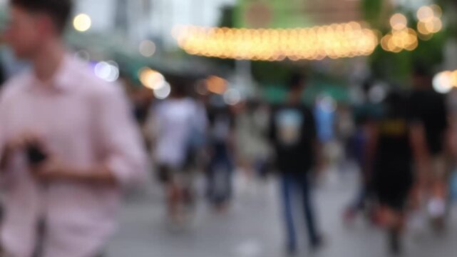 Bokeh view of street lights and blurred tourists. Crowds of Thai and foreign shoppers enjoy hanging out at Chatuchak Weekend Market, Bangkok. People walk, shop, eat, and take photos around the market.