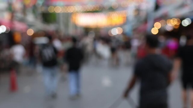 Bokeh view of street lights and blurred tourists. Crowds of Thai and foreign shoppers enjoy hanging out at Chatuchak Weekend Market, Bangkok. People walk, shop, eat, and take photos around the market.