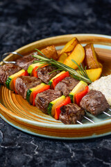 kebab on skewers in a plate with potatoes and sauce in a blue-yellow plate macro photo