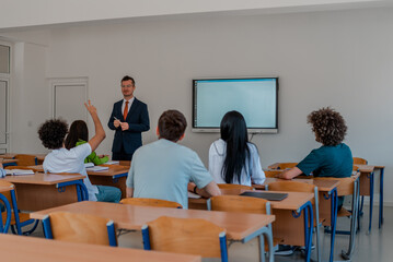 In the classroom, a group of college students listening to a university lecturer and engage in discussion and debate. The student raised a hand with a question for the teacher.