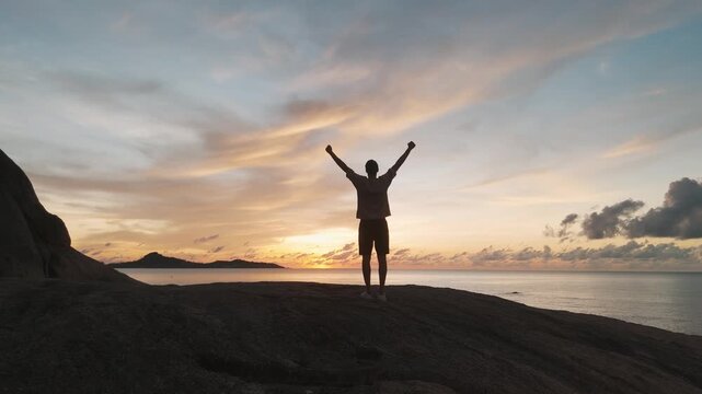 Figure on beach during golden sunset raising arms in delight grandeur of natural surroundings breathtaking sunsets. Man on seaside cliff at orange sunset arms raised in blissful enjoyment of moment.