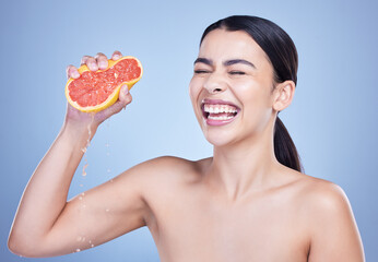 Happy woman, grapefruit and skincare with vitamin C for natural nutrition on a blue studio background. Female person or model with smile, squeeze or fruit for juice, detox or antioxidant in wellness