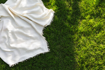 White picnic blanket on a green grass from top view