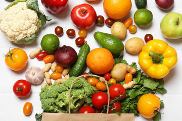 Vegan food delivery. Paper bag with different fresh vegetables, nuts and fruits on white tiled table, flat lay
