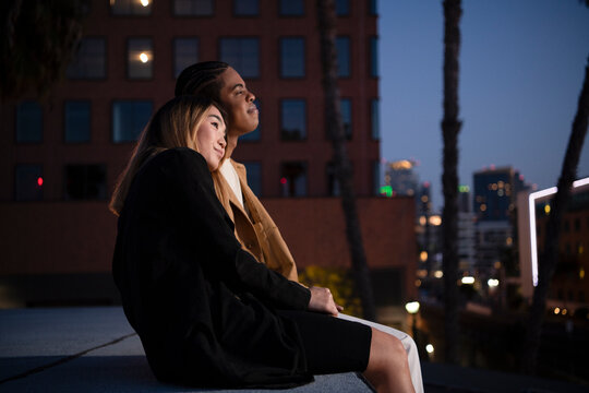 Multi racial couple snuggling embracing on urban rooftop at nigh