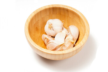 A wooden bowl filled with garlic (Allium sativum) ready to be used as a cooking ingredient. Photographed against a white background.