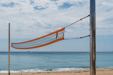 A weathered volleyball net stands before a calm ocean, symbolizing endurance and the passage of...