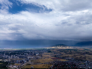 Drone view of a city near the mountains on a rainy day. Clouds over the mountains. Vibrant natural scenery.