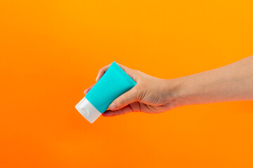 Blue cosmetic bottle, Skin care or sunscreen cosmetic in hand on orange background.