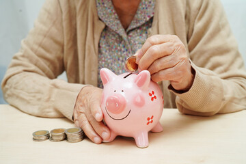 Retired elderly woman putting coins money in piggy bank and worry about monthly expenses and...