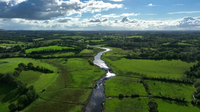 Finn River, County Monaghan, Ireland, September 2022. Drone pulls backwards in panoramic high angle overview of meandering water centered between pasture grasslands on sunny day.