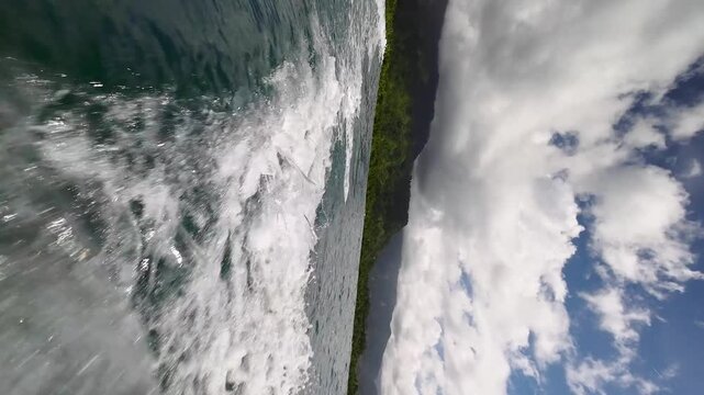 Vertical footage of boat wake leaving green tropical island coast