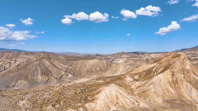Panoramic aerial rises above the eroded hills of Tabernas Desert and curves across the distinctive film industry landscapes crossing dry creek beds, craggy hills, and dust blown valleys.