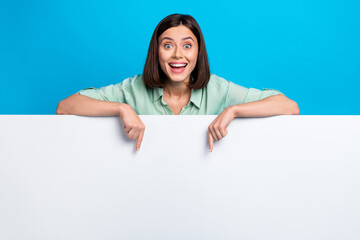 Photo of overjoyed woman dressed teal shirt indicating at awesome offer on billboard empty space isolated on blue color background © deagreez