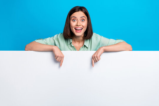 Photo of overjoyed woman dressed teal shirt indicating at awesome offer on billboard empty space isolated on blue color background