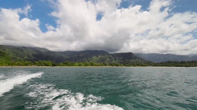 Tropical New Guinea coastline view from motorboat on sunny day with boat wake