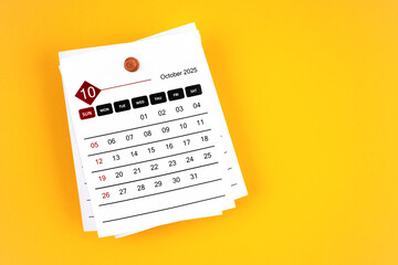 October 2025 calendar page with wooden push pin on yellow background.