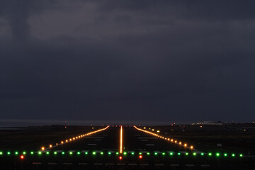 Empty airport runway at night, bathed in green and orange lights, guiding planes for safe takeoff and landing