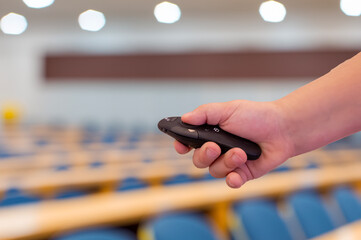 A lecture hall and a person holding a presentation remote control. Close-up.