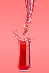 Red cherry juice. Stream of beverage flowing in drinking glass with bright splashes, drops flying, on pink background. Refreshing summer fruit drink for advertising, design, flyer, card, poster.