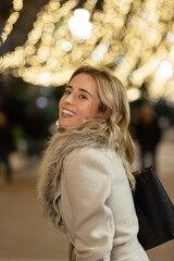 Portrait of
young woman strolling under the city christmas lights. She is happy and thoughtful on these special dates. Concept of family, friends, tradition, happiness, longing, shopping, loneliness.