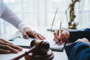 Lawyer holding pen is signing important legal contract with client in office with judge gavel and...