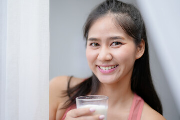 Young woman smiles happily while holding a glass of milk in her hands, embodying a healthy lifestyle in a cozy kitchen setting