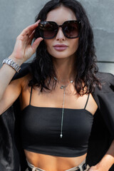 Naklejka premium Fashion pretty elegant curly woman in black stylish outfit with blazer and top wears sunglasses outdoors