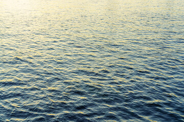 The texture of ripples on the water in a pond illuminated by the setting sun. Natural background.