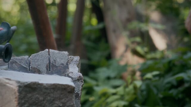 Cropped slowmo shot of unrecognizable male sculptor carving piece of natural stone with chisel and hammer while working outdoors