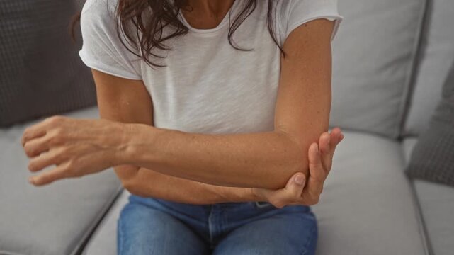 Mature woman experiencing elbow pain at home, showcasing discomfort and healthcare concepts.