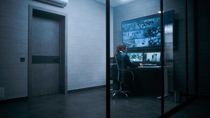 Female surveillance operator controls security cameras in modern monitoring center using computer....