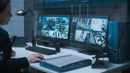 Multiple monitors and big digital screen showing surveillance video footage. Female dispatch or CCTV operator works on computer in monitoring center with security cameras, talks by walkie talkie.