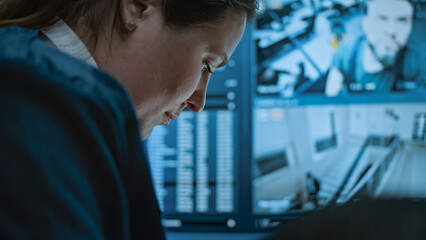 Multiethnic surveillance operators control security cameras on screens in monitoring center. Female security worker talks with African American male colleague, uses tablet computer with CCTV footage.