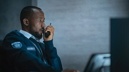 African American security officer or dispatch in uniform uses tablet computer and walkie talkie,...