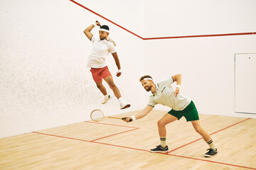 Man, friends and jump with squash racket for game, sports or intense match together in court. Young male person or athletic players in fitness, competition or training for smash, point or score