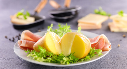 raclette cheese melted on potato with ham and lettuce on plate