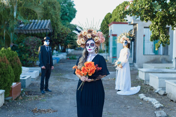 Group of three people made up as catrines in a cemetery. Day of the dead celebration.