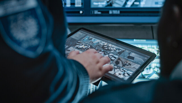 Female security officer talks with African American male coworker, uses tablet computer with surveillance footage. Diverse CCTV operators control security cameras on monitors in monitoring center. - Powered by Adobe