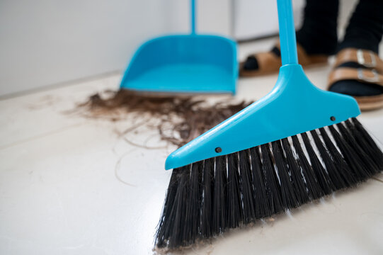Hairdresser sweeps up freshly cut hair from salon floor using broom and dustpan. View from floor level