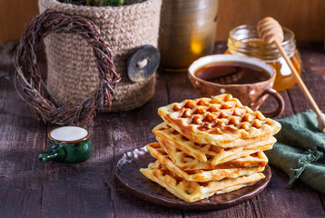 Belgian waffles served with honey, cream and sai on a wooden background. Rustic style.