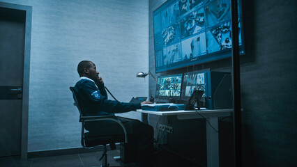 African American security worker monitors CCTV cameras in office on computer. Multiple monitors and...