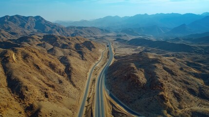Aerial shot of a long road cutting through a mountain range with varying elevations and clear skies. Perfect for journey and travel content