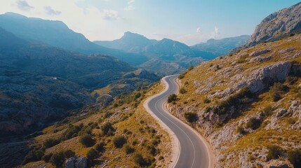 Fototapeta premium Aerial shot of a picturesque road through a mountain pass with clear skies and rocky terrain. Perfect for outdoor adventure themes