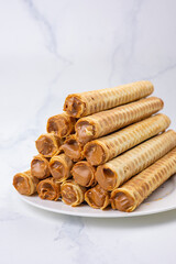 wafer rolls with chocolate and caramel on a white plate on a marble background
