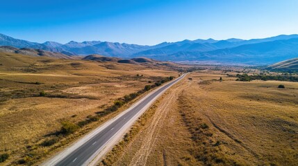 Aerial view of a picturesque road running parallel to a mountain range with clear skies. Perfect for landscape and travel conten