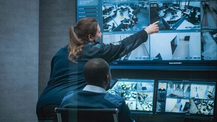 Female security worker talks with African American colleague, uses tablet. Multiethnic CCTV...