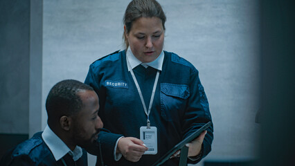 Female security worker talks with African American male colleague, uses tablet computer....