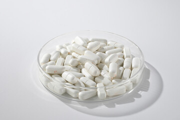 Minimalist photography with a transparent petri dish containing white pills isolated on a light white background. Samples of antibiotics, pain relievers, therapeutic drugs.
