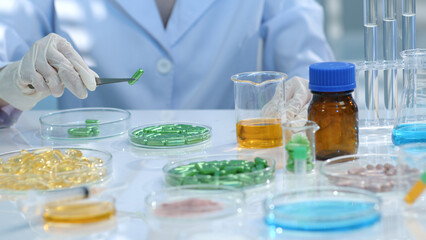 on the research table, many drug samples are stored in petri dishes. The researcher is using tweezers to pick up a green pill and examine it. Research landscape for medicinal products